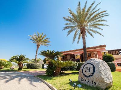 Hotel building with palm trees and large stone with logo on sunny grounds