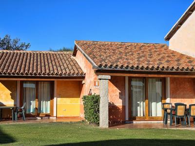 A house with orange facade, brown tiled roof, and shade on the green lawn.