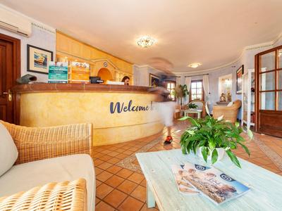 Bright reception area with counter, upholstered chairs, and a table with plants and magazines.