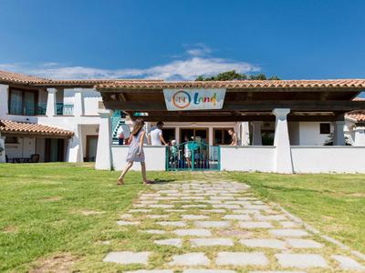 A hotel with white facade and red tile roof in sunny weather with green lawn in front.