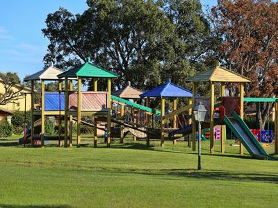 Colorful children's playground with slides and climbing equipment on a lawn in front of trees.