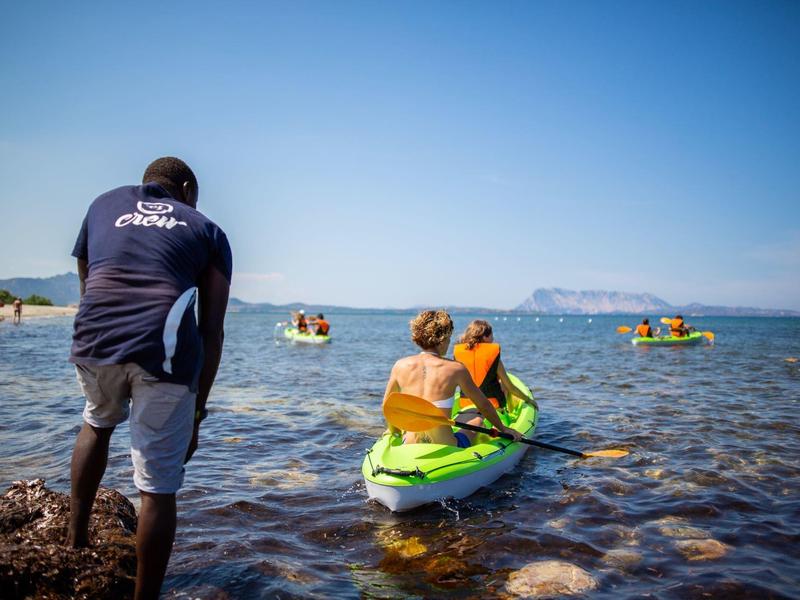 Person in water watching two people in a green kayak under clear sky.
