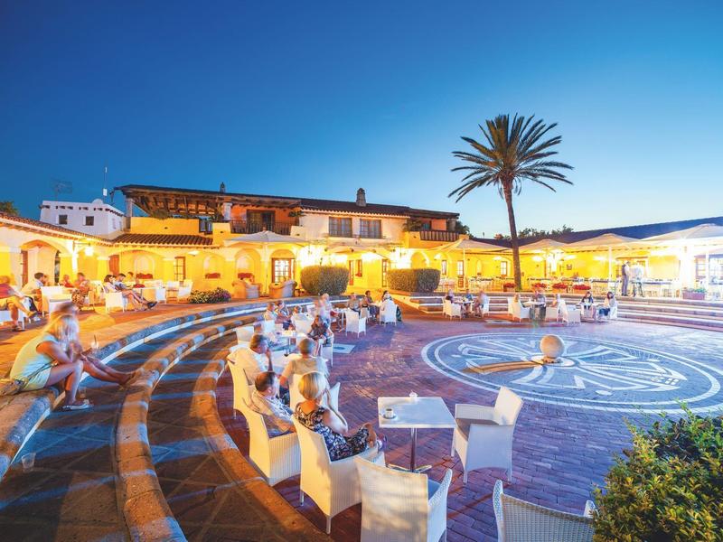 Illuminated courtyard with circular pattern and seating areas at sunset in a hotel.