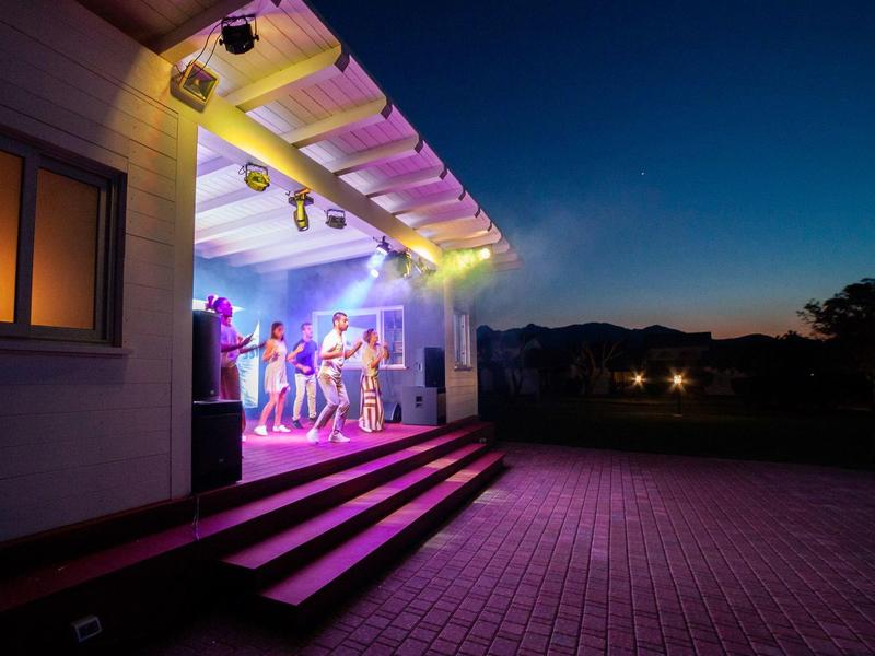 Evening party on a hotel terrace with colorful lights and people.