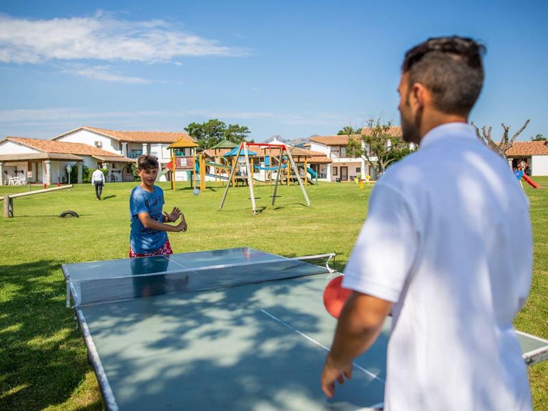 Two men playing table tennis in the garden of a holiday resort on a sunny day.