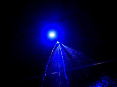 Blauwe waterfontein 's nachts tegen donkere lucht met helder lichtpunt.