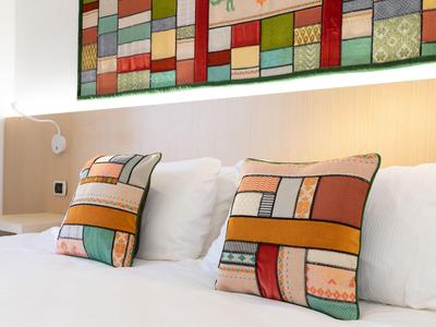 Wit bed met twee kleurrijke kussens en een kleurrijk wandkunstwerk in een hotelkamer.