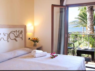 Lichte hotelkamer met tweepersoonsbed, balkondeur en zeezicht.