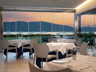 Modern restaurant met grote ramen met uitzicht op meer en bergen bij zonsondergang.