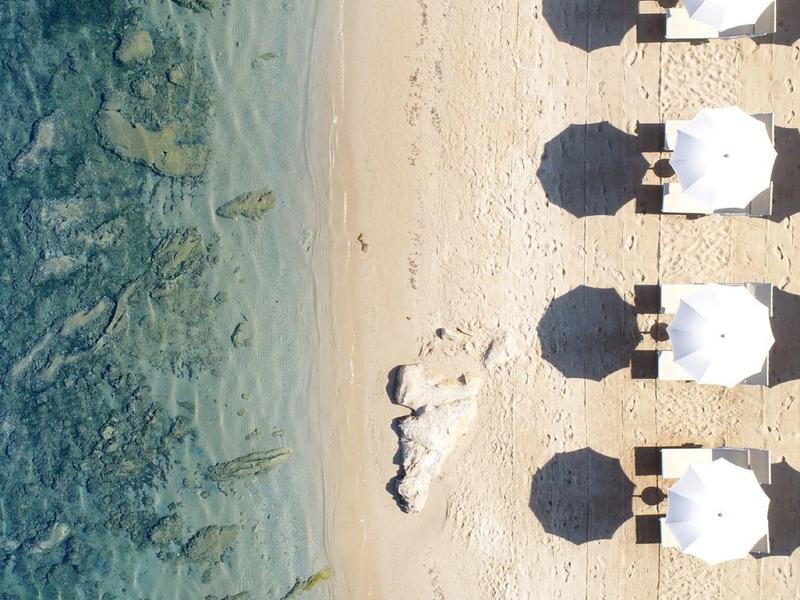 Luchtfoto van een strand met witte parasols en helderblauwe waterlijn.