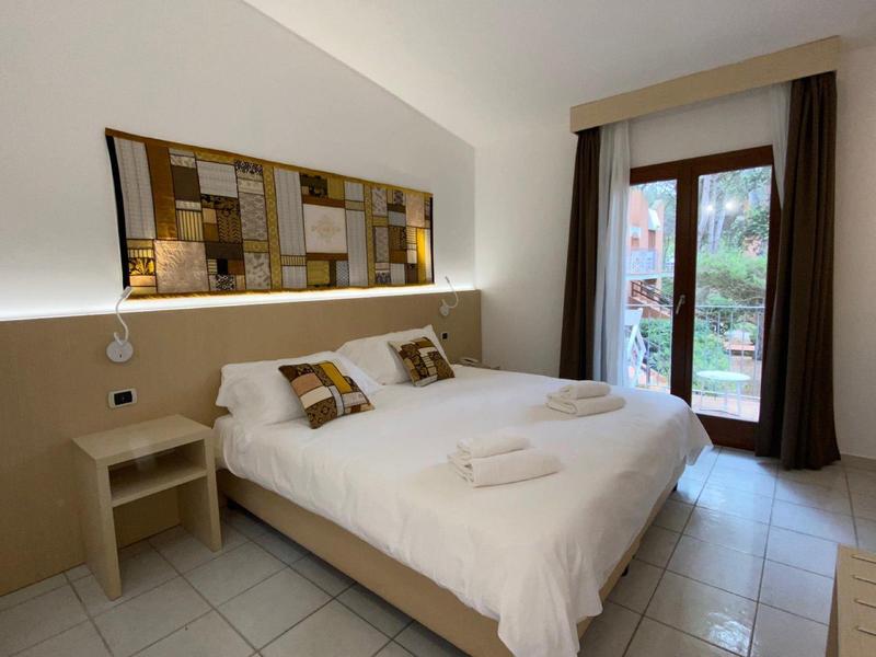 Moderne hotelkamer met tweepersoonsbed, nachtkastje, wanddecoratie en tuinzicht door raam met gordijnen.