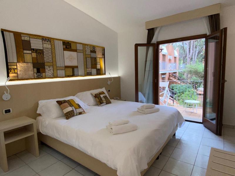 Heldere hotelkamer met groot bed en open balkon met uitzicht op tuin.