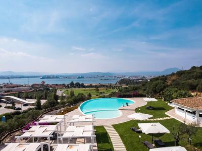 Hotelzwembad met witte ligstoelen, parasols en uitzicht op zee en landschap.
