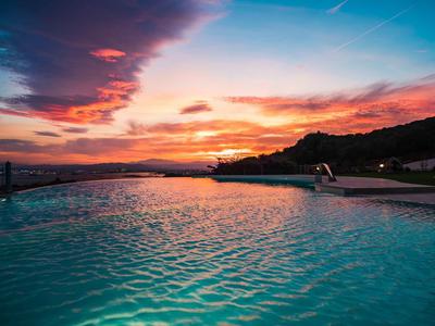 Infinity-zwembad met uitzicht op een kleurrijke zonsondergang boven heuvels aan zee.