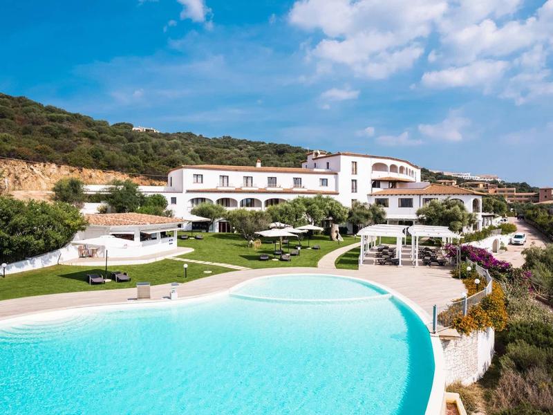 Groot hotel met witte gevel en een groot zwembad in een zonnige omgeving.