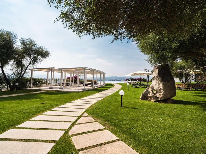 Een verzorgd wandelpad leidt door groen gras naar witte paviljoenen met uitzicht op zee.
