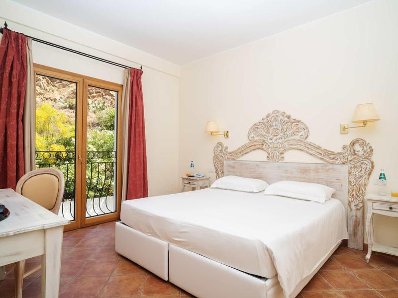 Lichte tweepersoonskamer met sierlijk hoofdeinde en balkon met uitzicht op groen.