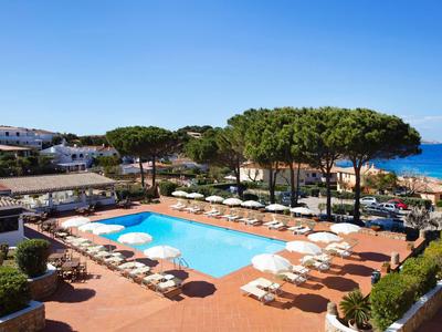 Hôtel avec grande piscine, terrasse, chaises longues et vue sur la mer sous un ciel clair.
