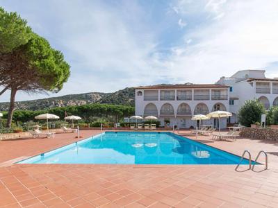 Grand piscine avec eau claire devant un bâtiment d'hôtel à plusieurs étages et des arbres en arrière-plan.