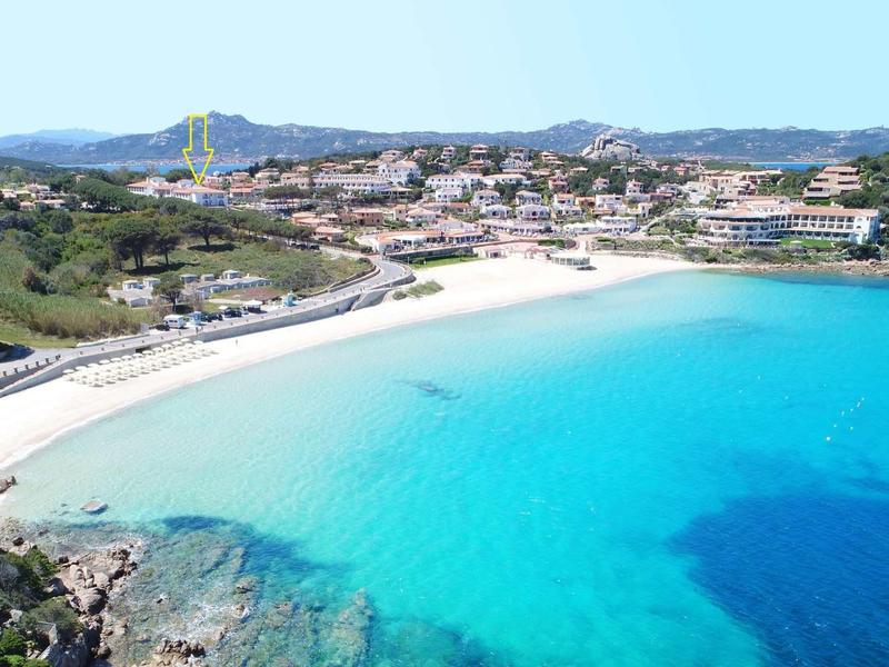 White sandy beach with clear blue water and hotels in the background under sunny weather.
