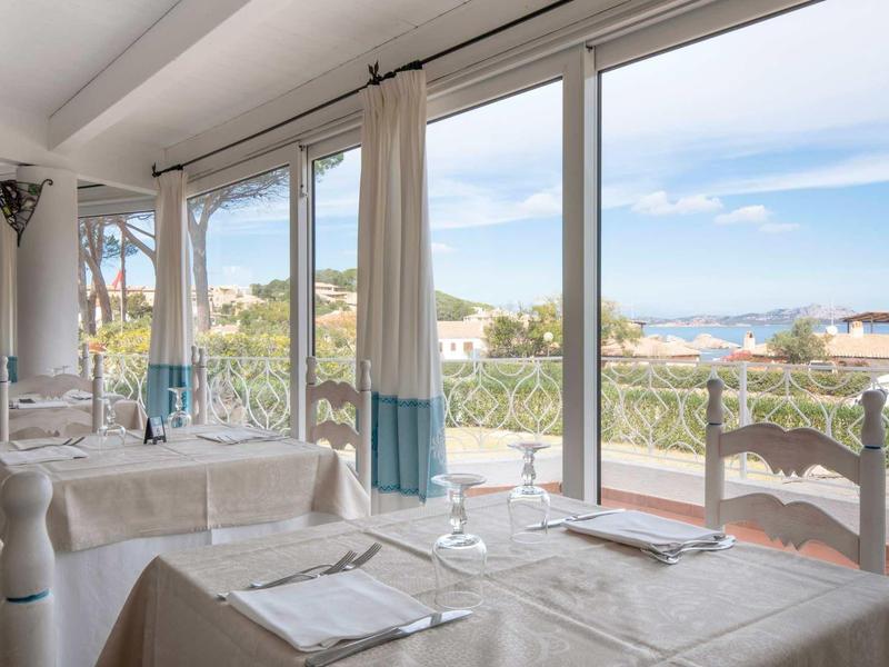 Bright dining room with set tables and large window overlooking the sea.