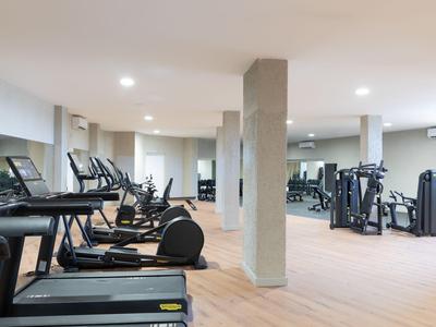 Grande salle de sport d'hôtel avec tapis roulants et divers appareils d'entraînement sur un sol en bois clair.