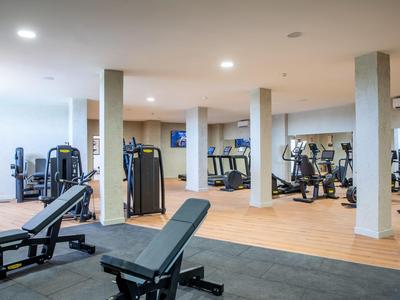 Salle de sport moderne d'hôtel avec plusieurs appareils de musculation et miroirs aux murs.