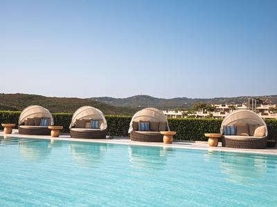 Área de piscina de lujo con camas redondas y vistas a colinas bajo cielo despejado.