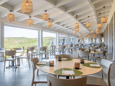 Restaurante luminoso con grandes ventanas y muebles de madera con vista a un paisaje verde.