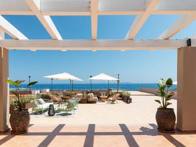 Vista da una terrazza con colonne bianche su una spiaggia soleggiata con ombrelloni e mare blu.