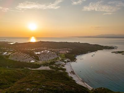 Vue aérienne d'un hôtel côtier au coucher du soleil avec plage et mer calme.