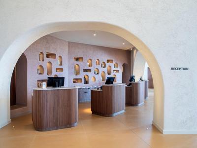 Moderner Hotel Empfang mit runden Holztresen und dekorativen Wandnischen unter einem großen Bogen.