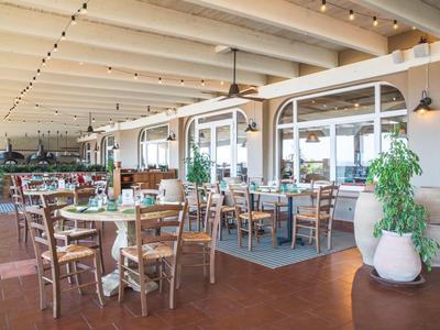 Helles Restaurant mit Holztischen, Stühlen und großen Pflanzen in Töpfen.