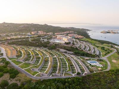 Luftaufnahme eines Resorts am Meer mit Reihen von gebogenen, weißen Gebäuden und grüner Umgebung.