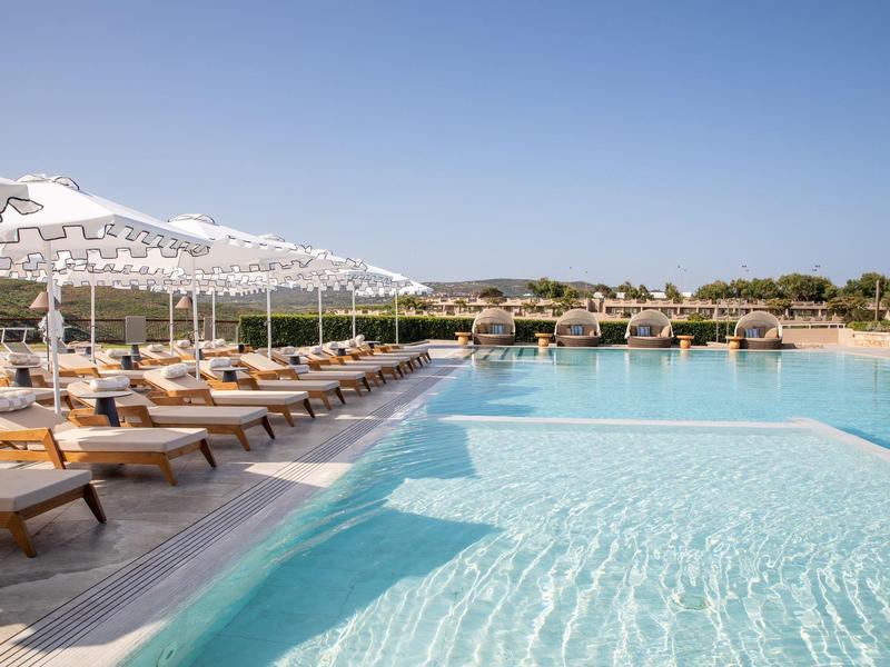 Ein großer Hotelpool mit Liegestühlen und Sonnenschirmen an einem sonnigen Tag.