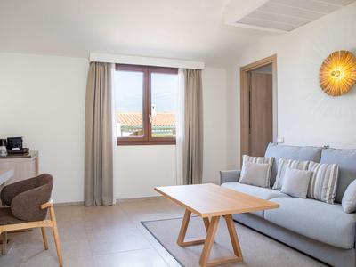 Moderní obývací pokoj se šedou pohovkou, dřevěným stolem, šedým křeslem a oknem se závěsy.