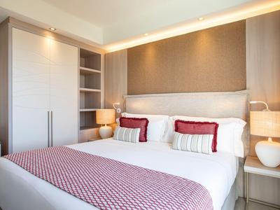 Moderní hotelový pokoj s manželskou postelí, nočními stolky, lampami, světlým dřevem a bílými tóny.