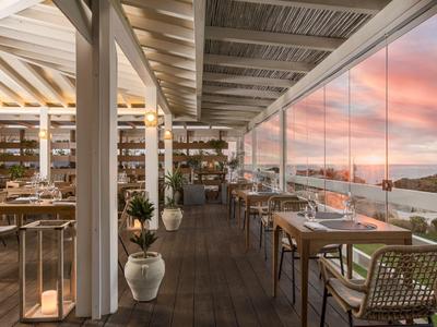 Terasa restaurace s dřevěnou podlahou a výhledem na západ slunce nad vodou