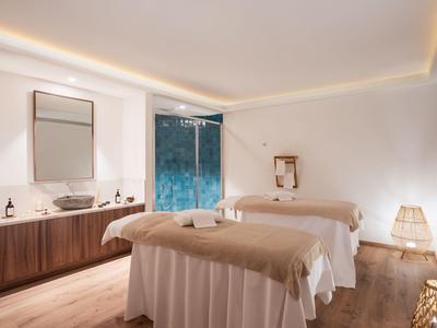 Sala de spa luminosa con dos camillas y una gran ventana con vista a la naturaleza.