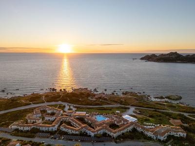 Západ slunce nad přímořským hotelovým resortem s bazénem a několika budovami.