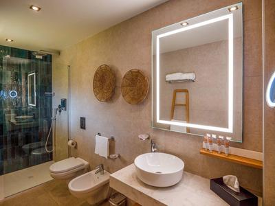 Modernes Badezimmer mit beleuchtetem Spiegel, Waschbecken, WC, Bidet und begehbarer Dusche.