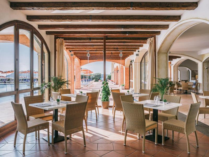 Otevřená restaurace s výhledem na terasu, dřevěné židle a dekorativní rostliny.