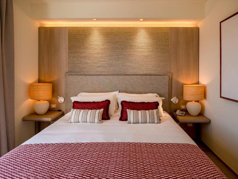 Moderní ložnice s manželskou postelí, červenými polštáři a teplým osvětlením, útulná a příjemná.