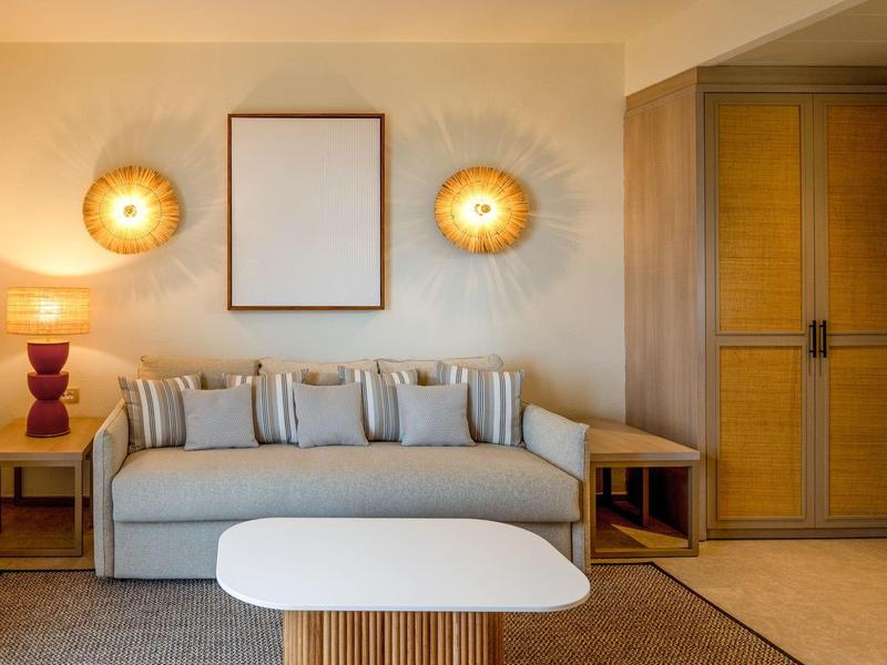 Moderní hotelový pokoj se šedou pohovkou, stolem a teplým nástěnným osvětlením.