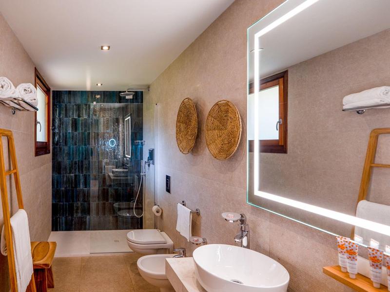 Moderní koupelna se svítícím zrcadlem, volně stojícím umyvadlem a sprchovým koutem.