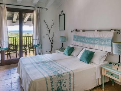 Camera luminosa con letto matrimoniale, balcone e vista su un lago e colline verdi.