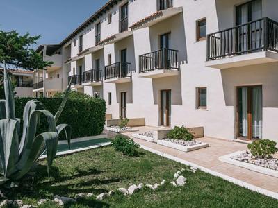 Witte hotelgebouwen met balkons en een tuin met planten en gras.