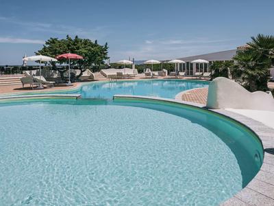 Piscina rotonda con acqua limpida e lettini bianchi in un giardino d'hotel