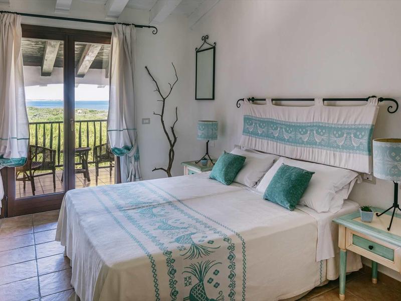 Camera luminosa con letto matrimoniale, balcone e vista su un lago e colline verdi.