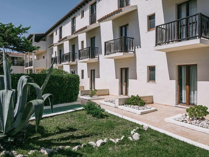 Un edificio bianco dell'hotel con balconi e un piccolo giardino con piante e verde.